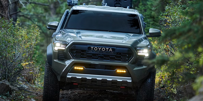 Toyota off-road truck driving through a narrow forest trail.